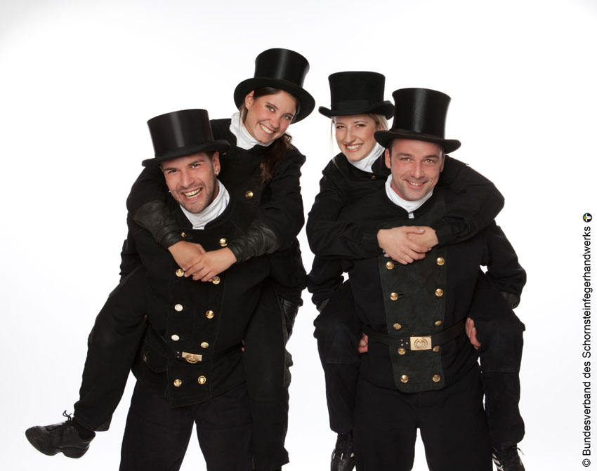 Vier Schornsteinfegerinnen und Schornsteinfeger im traditionellen Zylinder des Schornsteinfegerhandwerks